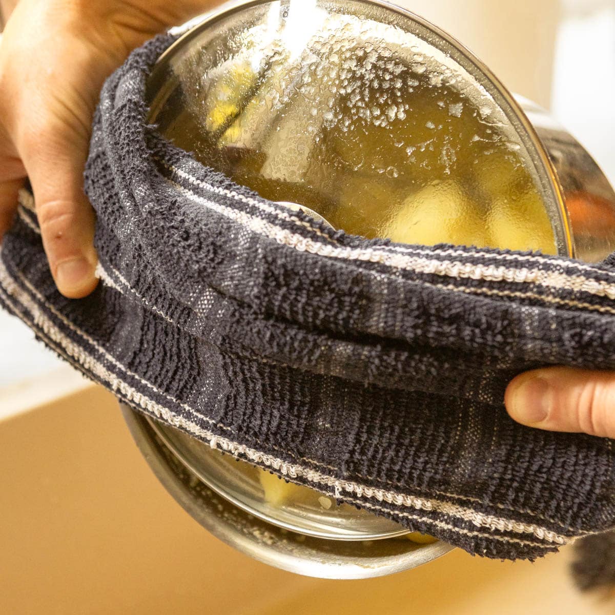 A pot with potatoes being drained above a sink.