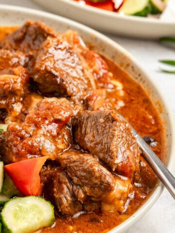 Greek beef stifado served along fresh Greek salad, with a fork submerged.