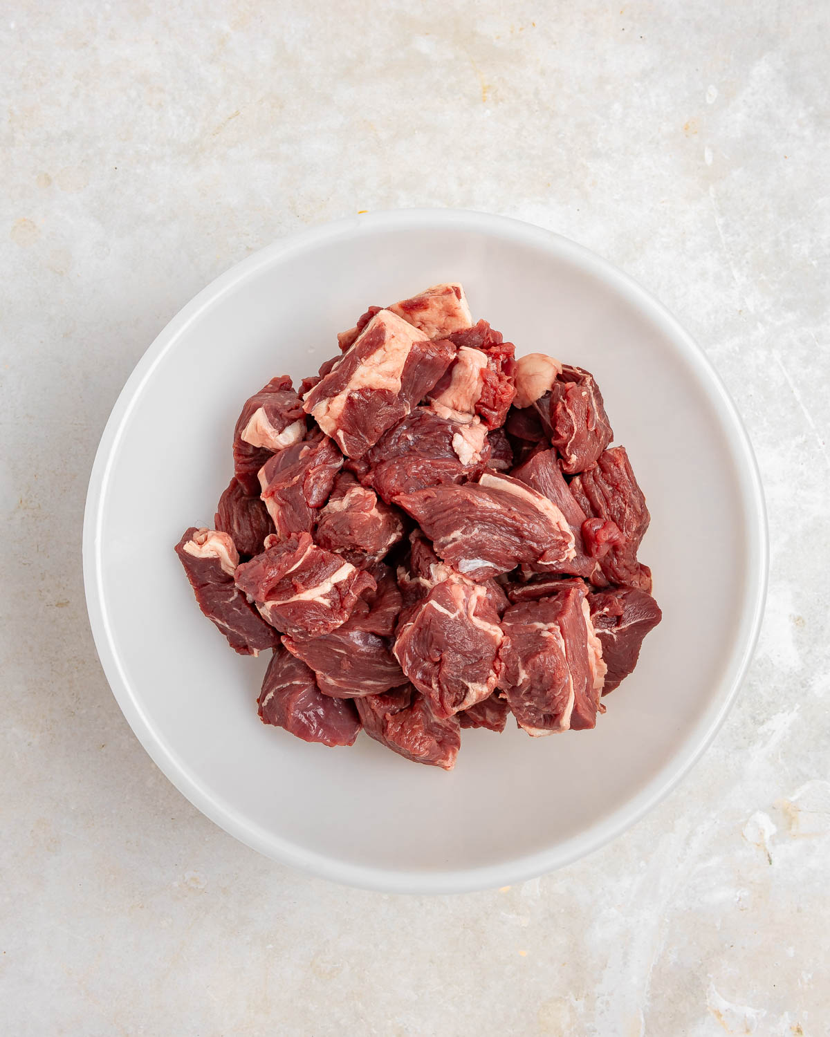 A round white bowl with beef cut into cubes.