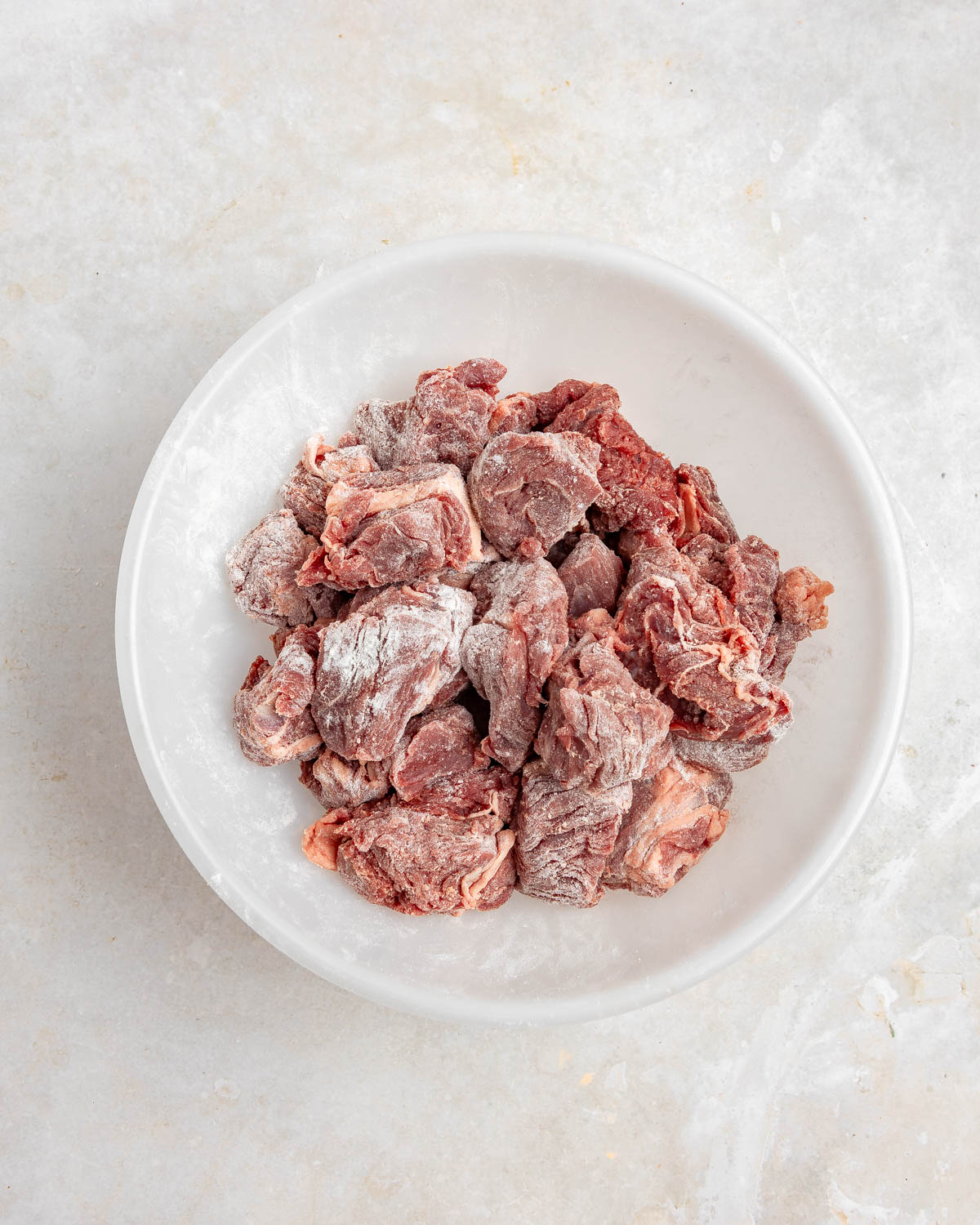 A round white bowl with chunks of beef coated in a flour mixture.