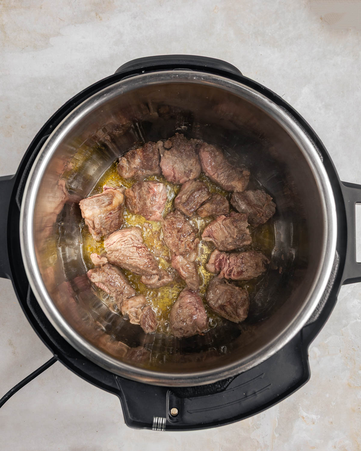 An open Instant Pot with beef chunks being fried.