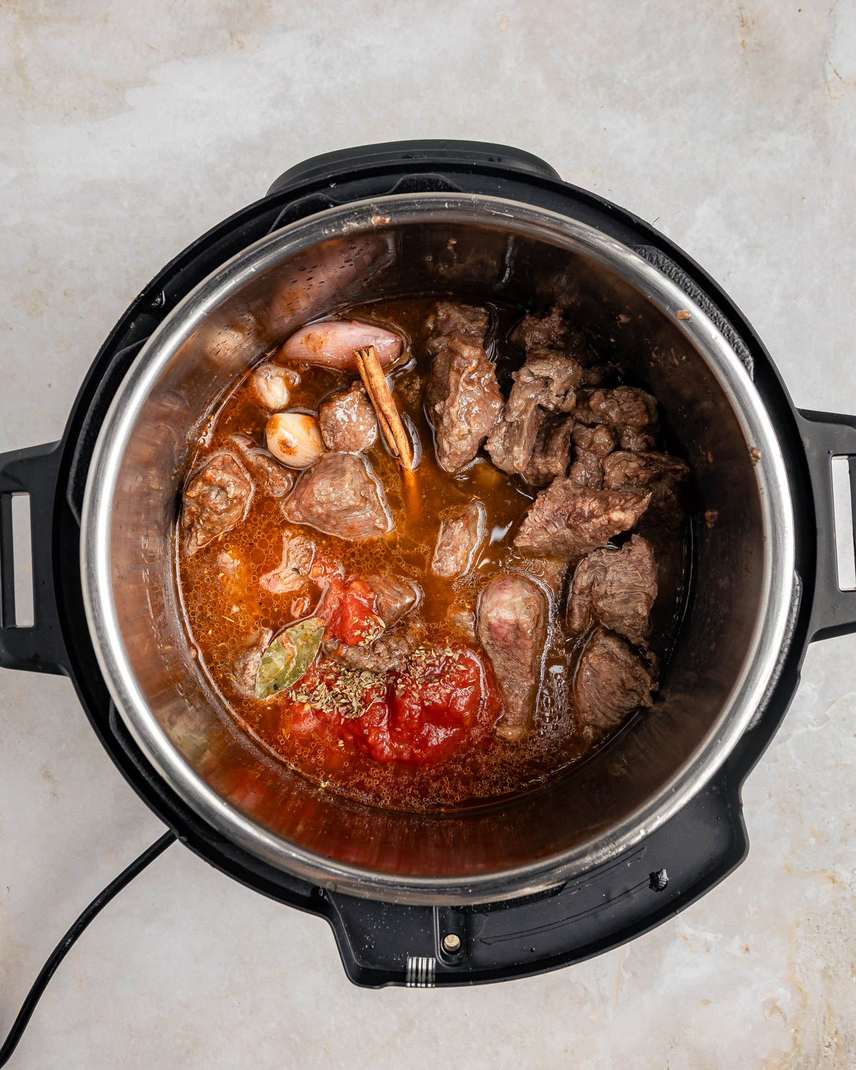 A top-down view of an instant pot with beef stifado ingredients inside.